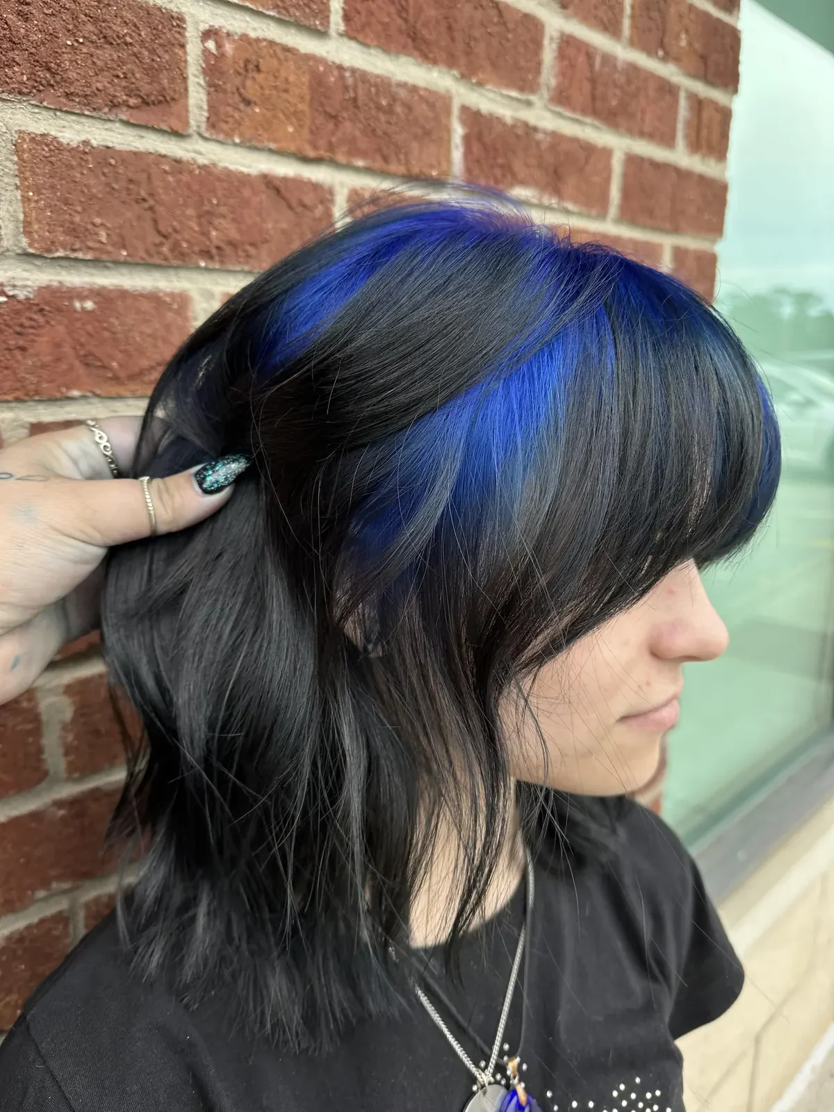 Side profile of a woman with a medium black layered shag and a blue peekaboo panel near the roots.