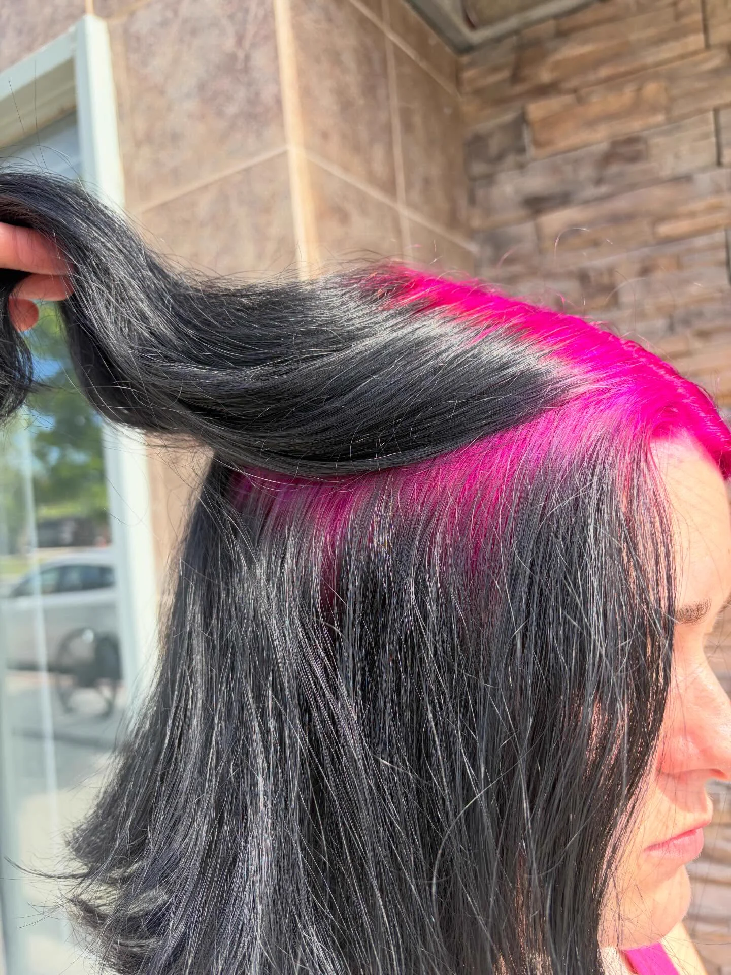 Close side view of straight black hair lifted to reveal a broad hot-pink underlayer at the temple and side roots.