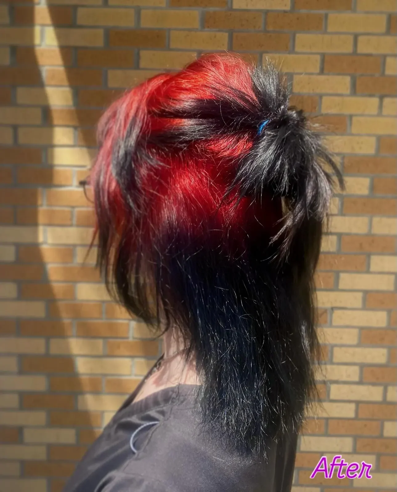 Back view of a woman wearing long black hair up with red color visible across the top roots.