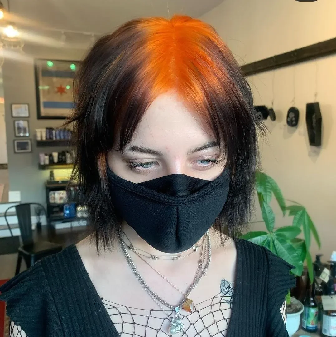 Woman with a medium black shag and red roots visible through a split fringe.