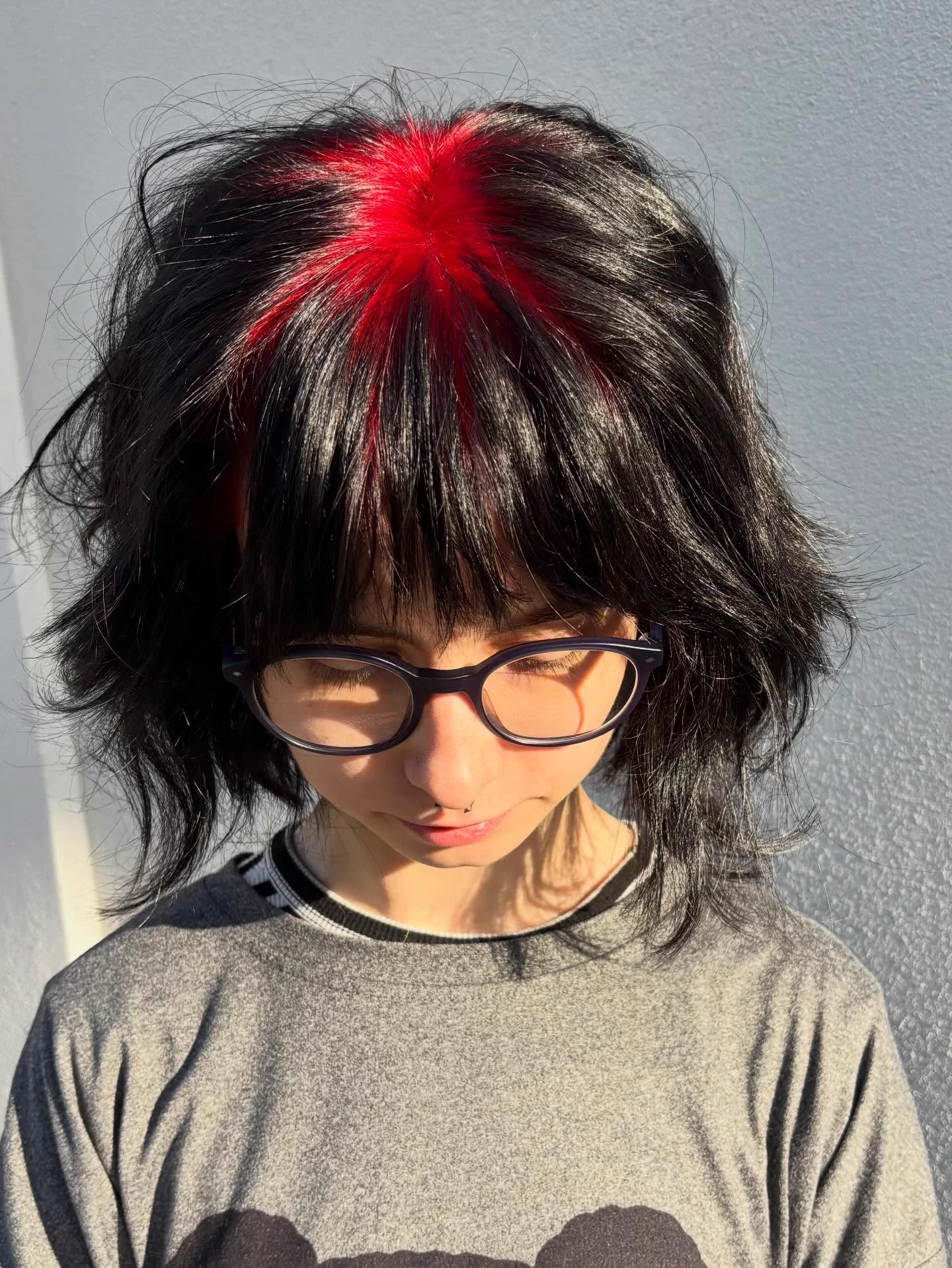 Top-down view of a woman with medium black waves and red color bursting from the center crown toward the fringe.