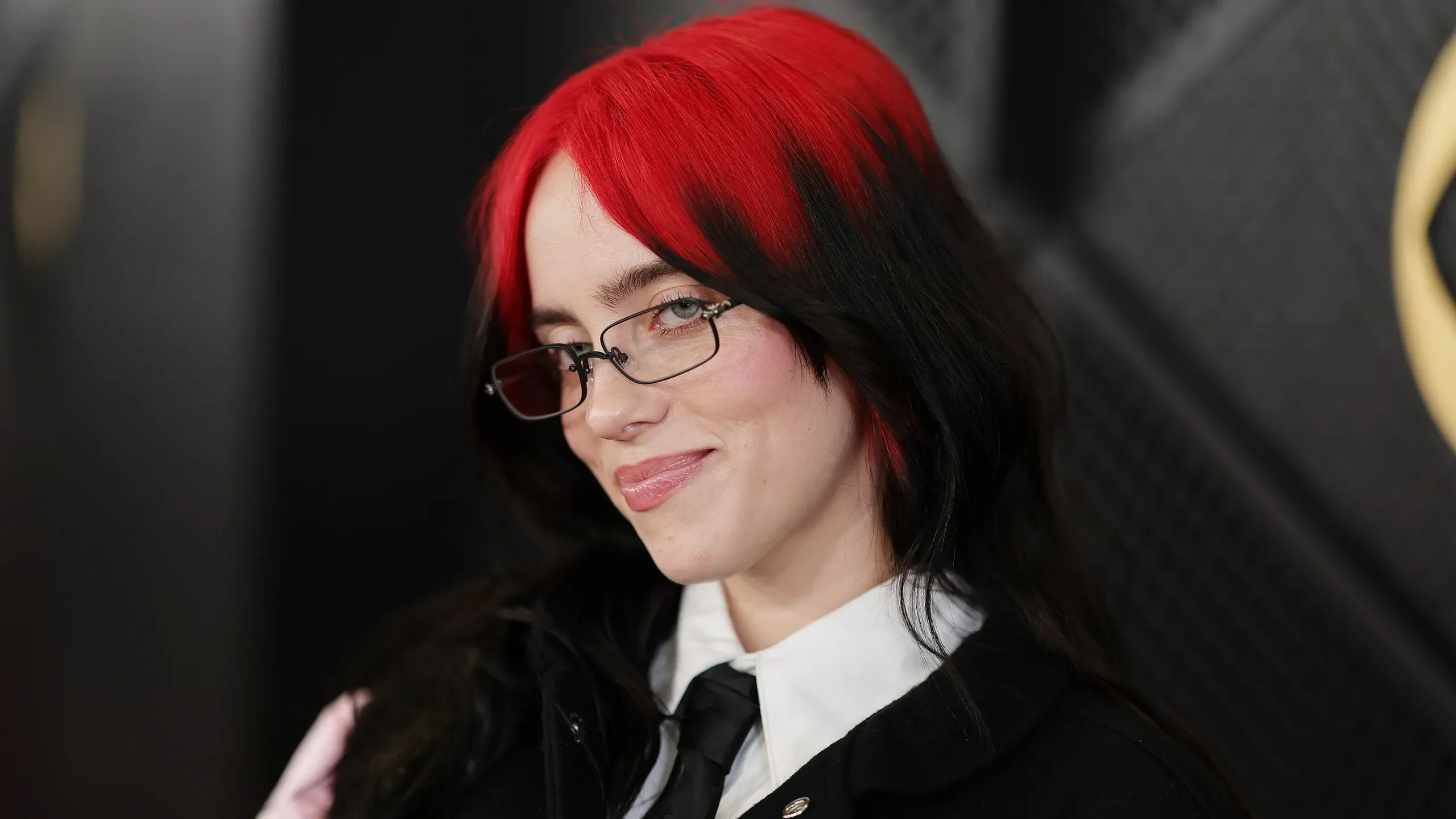 Side portrait of a woman with a short sleek black bob and red roots through the split fringe.