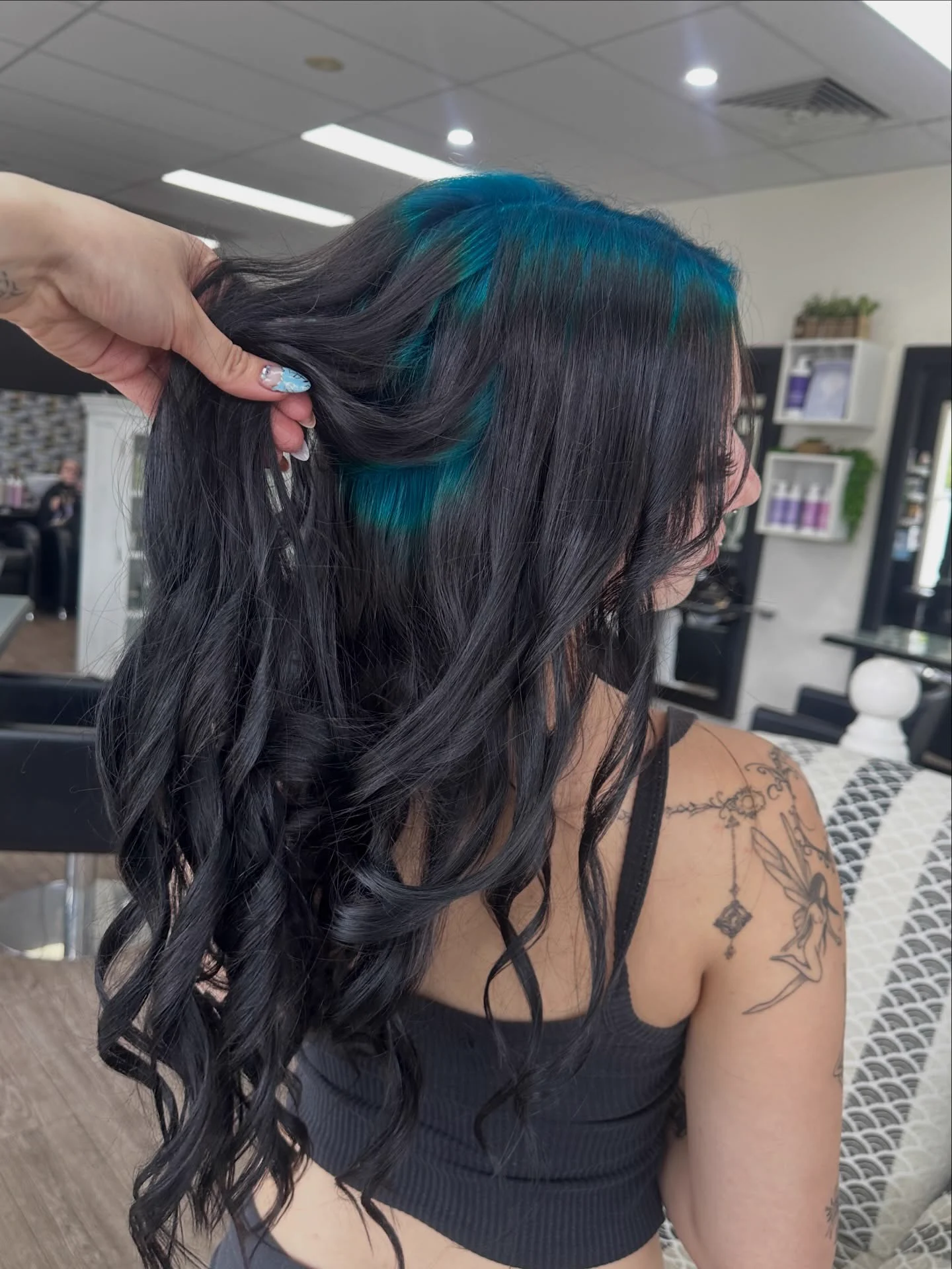 Long black wavy hair lifted to reveal a teal root halo beneath the surface layer.