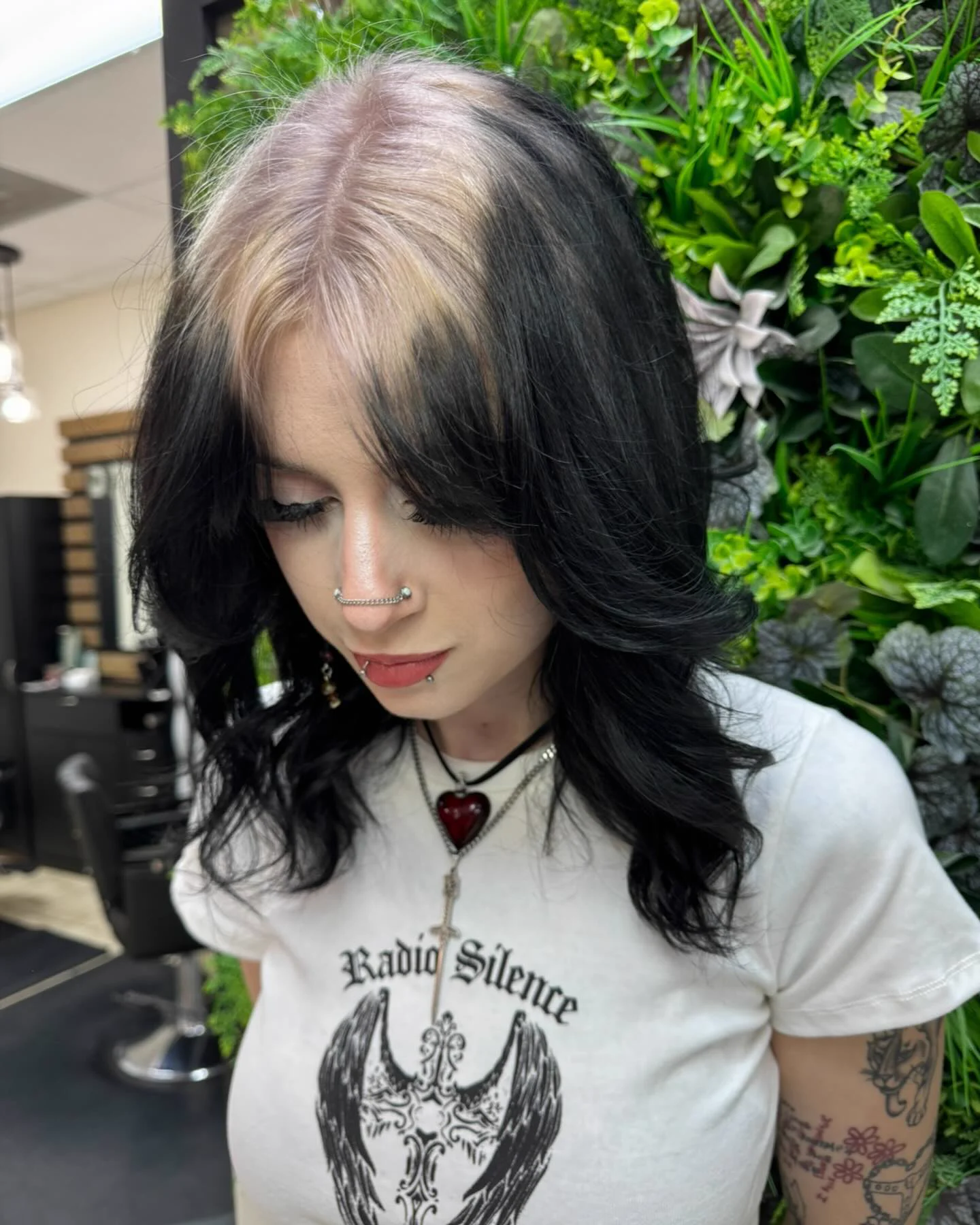 Woman with medium black wavy hair and a platinum-white root panel following the center part.