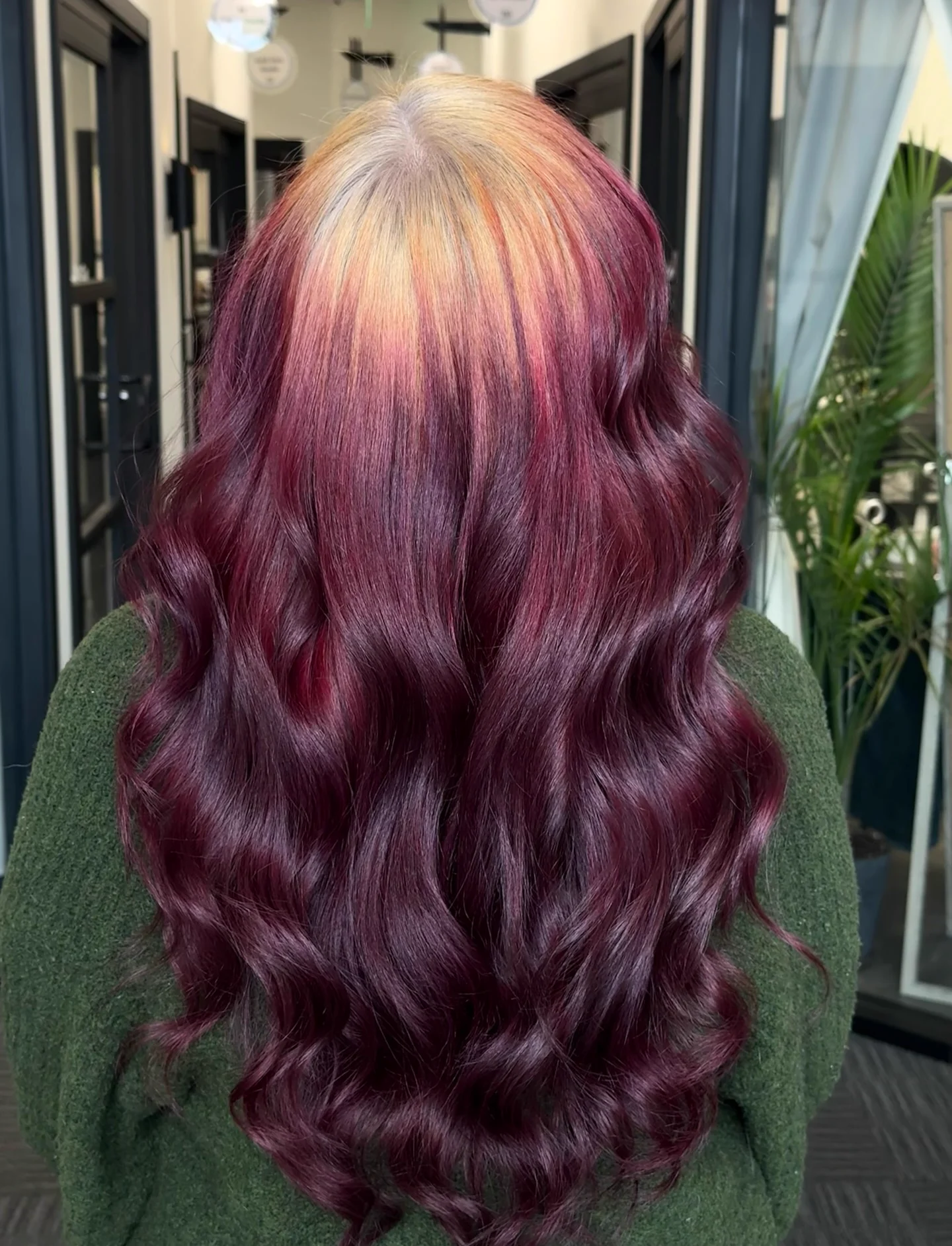 Back view of long red wavy hair with broad blonde roots softly blended across the crown.